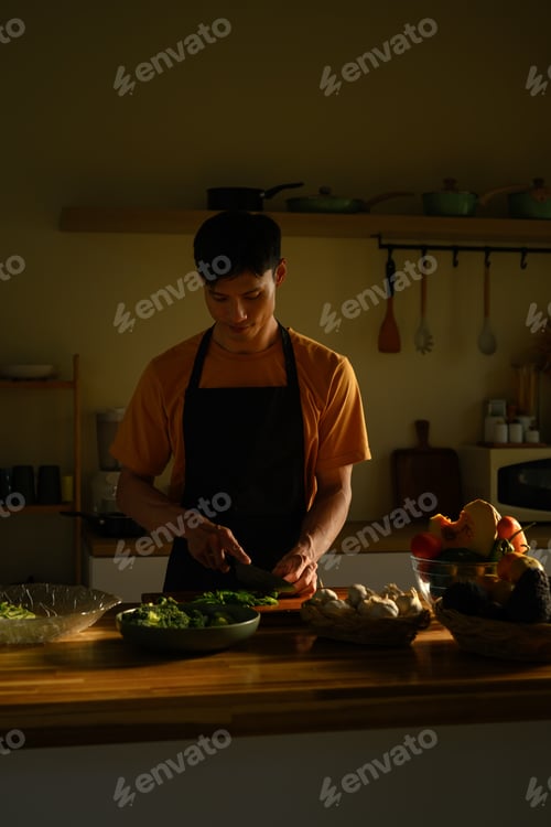 Preview: Man slicing green chili on a wooden board in a kitchen, showing careful food preparation