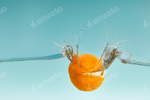 Preview: cut orange falling in water with splashes on blue background