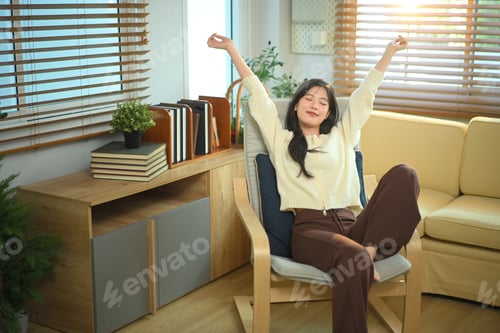 Preview: Happy relaxed young woman resting sitting on comfortable armchair in living room