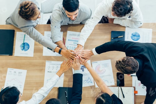 Preview: Colleagues stacking hands above table with papers