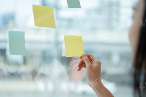 Preview: Close-up image of a businesswoman attaching or looking at a sticky note on a glass wall.