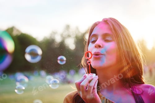 Preview: Young woman covered in coloured chalk powder blowing bubbles at Holi Festival