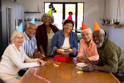 Preview: Portrait of cheerful multiracial senior friends wearing party hats and woman holding cupcakes