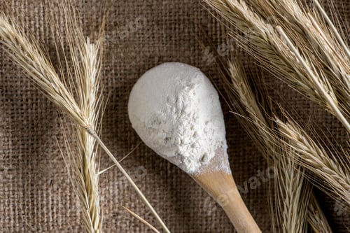 Preview: close up view of flour in wooden spoon and wheat on sackcloth
