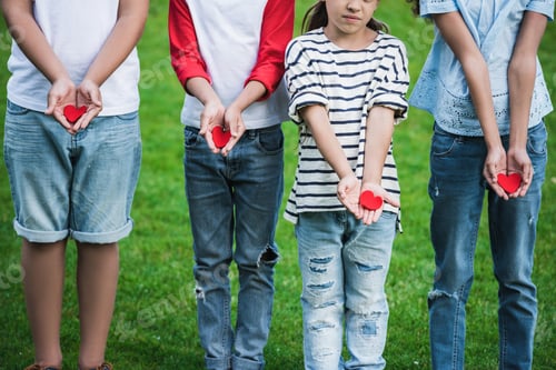 Preview: Cropped shot of cute little children holding red hearts while standing on green grass
