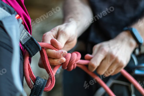Preview: Alpinist tying a rope on his climbing equipment