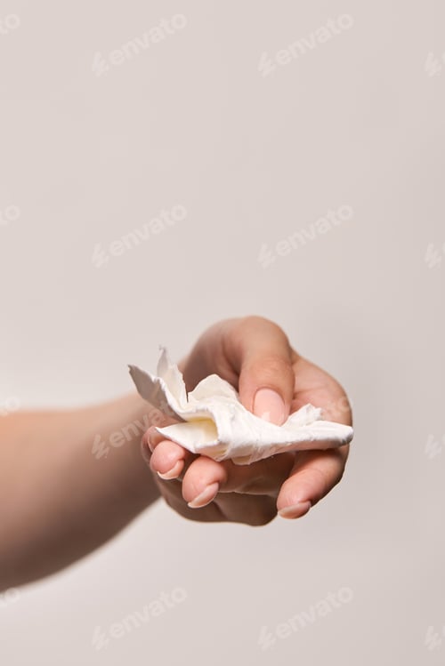 Preview: Female hand holding crumpled tissue against neutral background close-up
