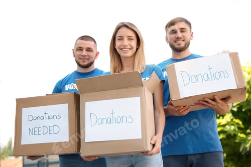 Preview: Young volunteers holding boxes with donations for poor people outdoors