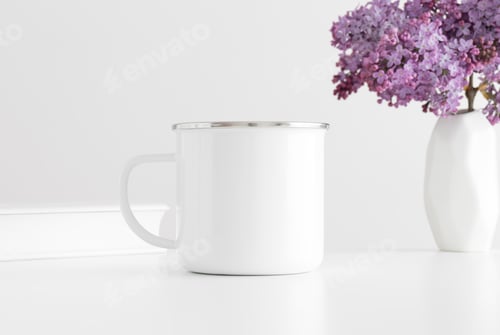 Preview: Enamel mug mockup with a book and a bouquet of lilac in a vase on a white table.