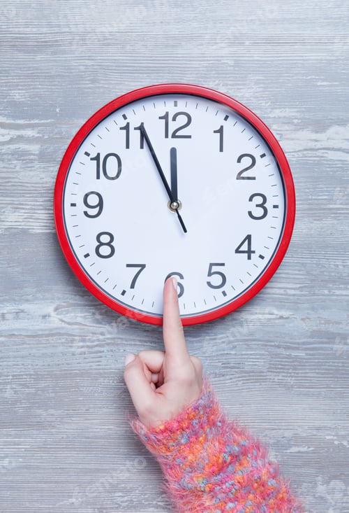 Preview: Female hand holding clock on a table.
