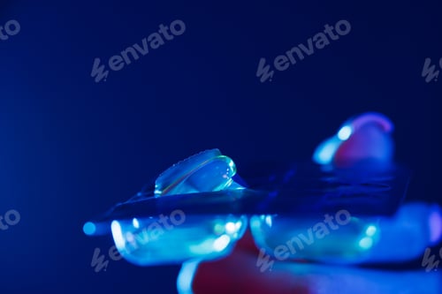 Preview: hand holding pills or drugs close up in ultraviolet color