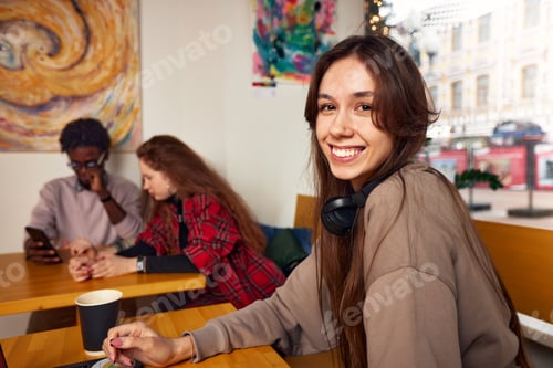 Preview: Young smiling female student using laptop for e-learning in headphones, watching online seminar in