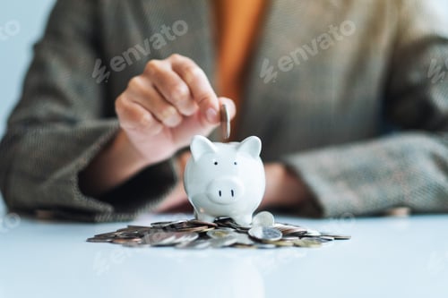 Preview: A businesswoman putting coin into piggy bank with pile of coins on the table for saving money