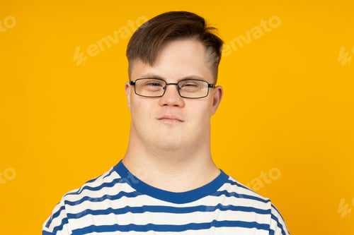 Preview: Smiling young man with cerebral palsy in glasses in a striped t-shirt on a yellow background