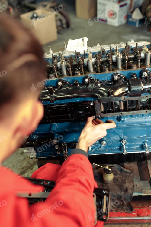 Preview: Vertical closeup of a mechanic in a red uniform mounting the car engine