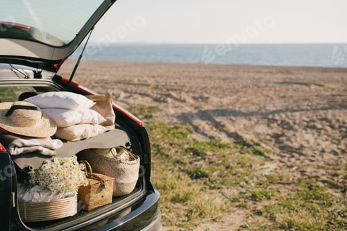 Preview: Car with opened trunk with picnic items: basket, pillows, blanket, straw hat. Summer vacation.