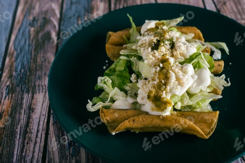 Vista previa: Tacos flauta with cheese, cream and lettuce on a wooden table. Mexican snacks.