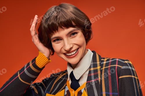 Preview: happy college girl with short hair posing in her uniform on orange background, high school