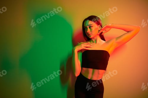 Preview: Green and red colors. Fashionable young woman standing in the studio with neon light