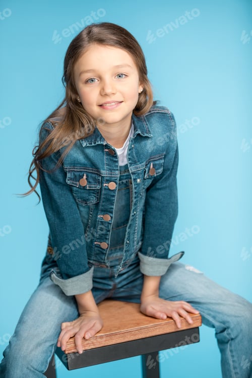 Preview: portrait of little girl smiling and sitting on stool in studio isolated on blue