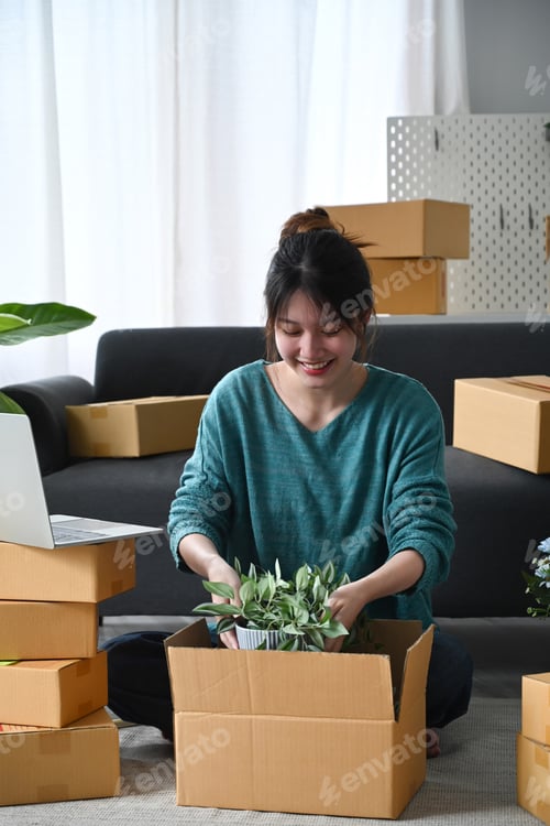 Preview: Young woman small business owner packing product in cardboard box for delivery to customers.