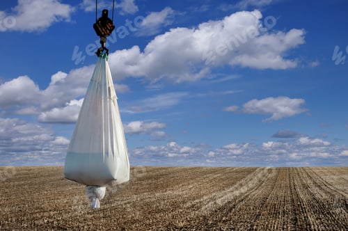 Preview: bag of seeds or mineral fertilizers at crane on field before sowing