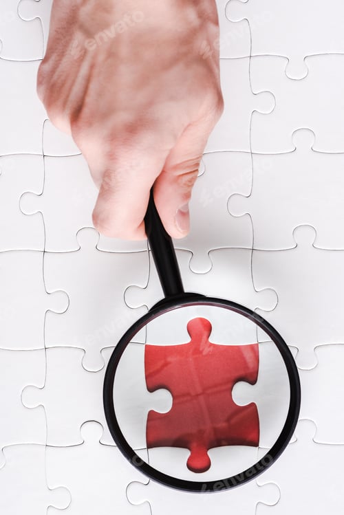 Preview: top view of man holding magnifying glass near red jigsaw near white connected puzzle pieces