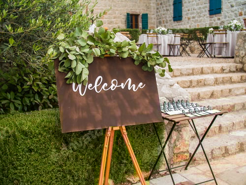 Preview: Welcome inscription on wooden board in green garden background on wedding ceremony. Rustic