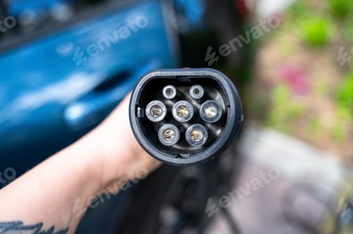 Preview: Hand holding EV charging plug near car in private yard