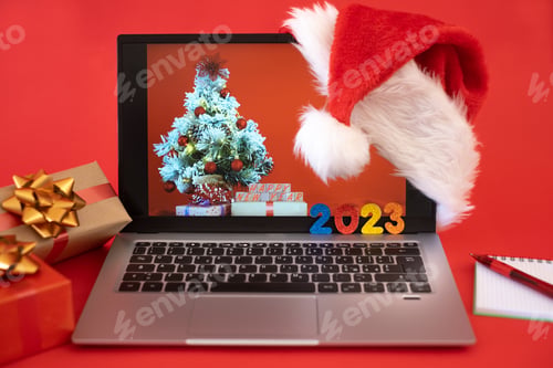 Preview: Desk with laptop at Christmas time, message of happy new year 2023 - red background