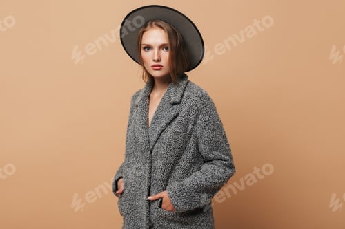 Preview: Young attractive lady with wavy hair in gray hat and coat holding hands in pockets