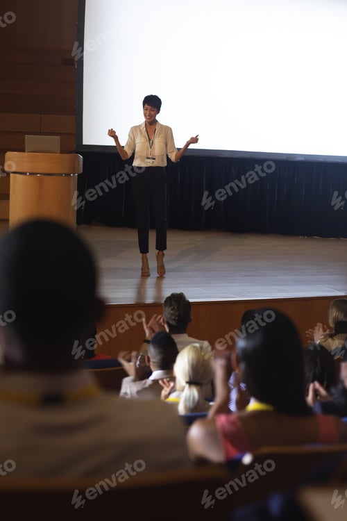 Preview: Beautiful businesswoman standing and giving presentation in front of the audience in auditorium