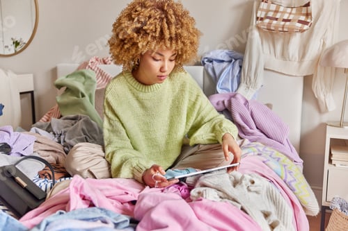 Preview: Photo of curly haired woman uses tablet for making shopping online checks ecommerce clothing store