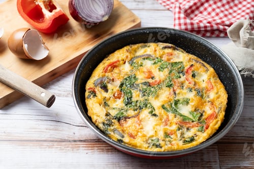 Preview: Italian Frittata made with spinach, tomatoes, onion and peppers on white wooden table