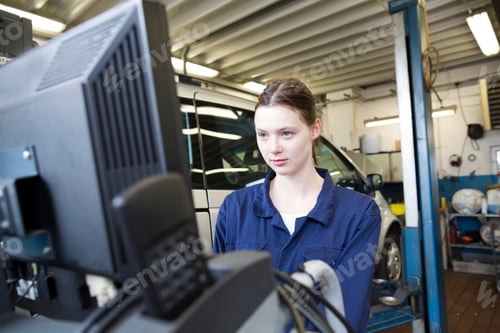 Preview: Young woman in repair garage checking car with electronic control