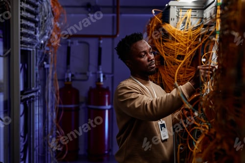 Preview: Black young man as system administrator working with server in neon light
