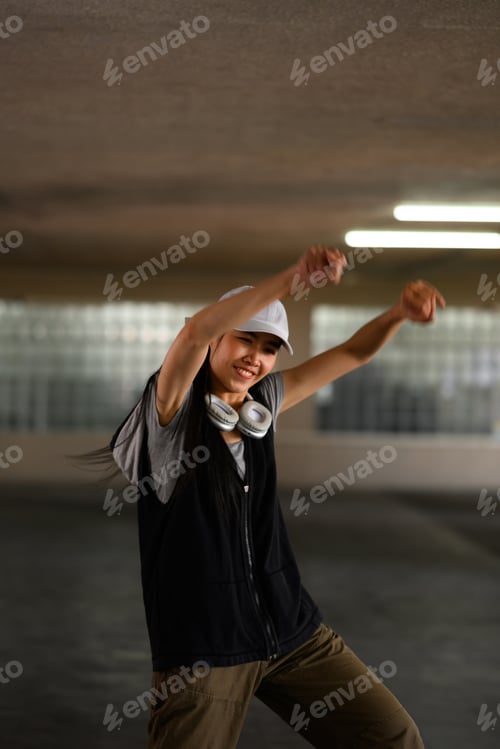Preview: Smiling young woman dancing, doing hip hop movement in parking lot.