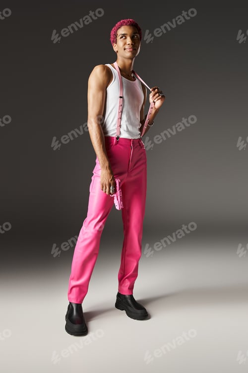 Preview: handsome african american male model posing in vibrant outfit and holding toy gun on gray backdrop