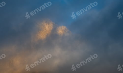 Preview: Foggy rocky mountain landscape at sunrise with blue sky.
