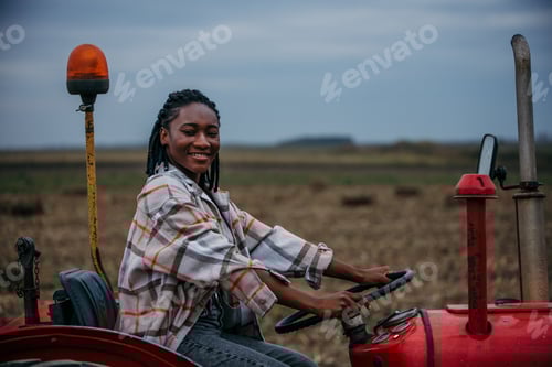 Visualização: Jovem agricultora dirigindo trator vermelho no campo após a colheita