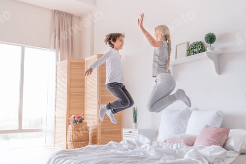 Preview: Happy kids jumping, having fun, playing on bed in bedroom enjoying of morning