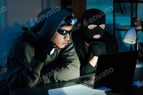 Preview: Two Young Adult Men Wearing Masks Hacking Computer in Office at Night