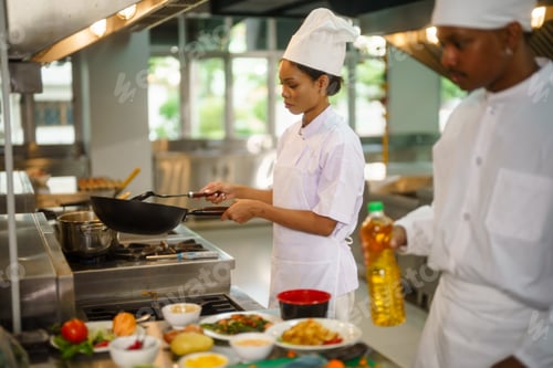 Preview: Two chefs in uniform working in a professional kitchen, one cooking with a wok