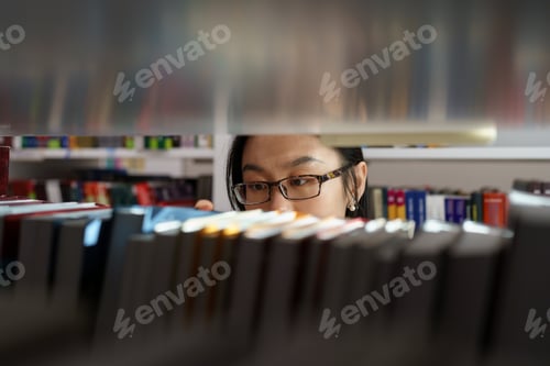 Preview: Asian student girl studying in university library. Young woman picking book from shelf for project