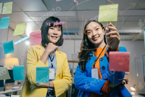 Preview: Two asian businesswomen are using colorful sticky notes and a marker pen, working together on a proj