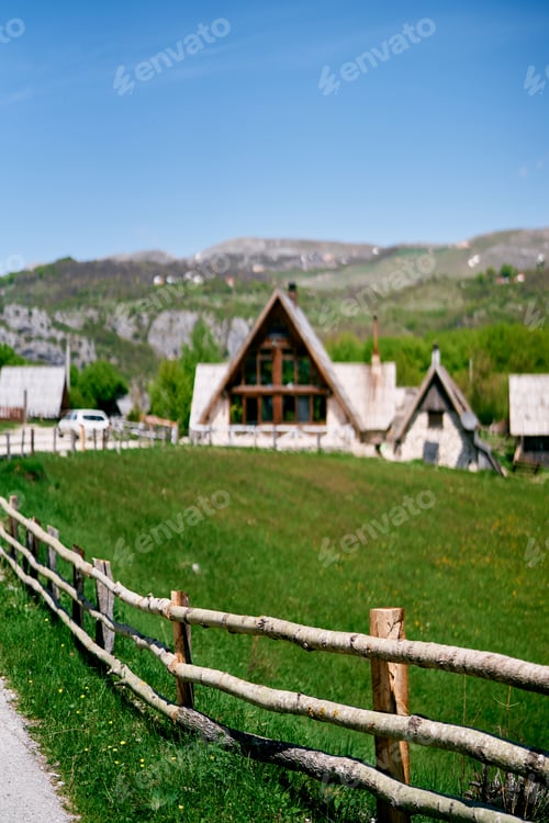 Preview: Triangular houses in a green valley behind a wooden fence along the road at the foot of the