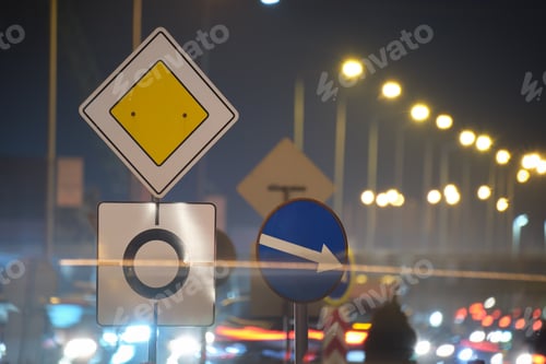 Preview: Roundabout road signs with blurred cars on city street traffic at night.