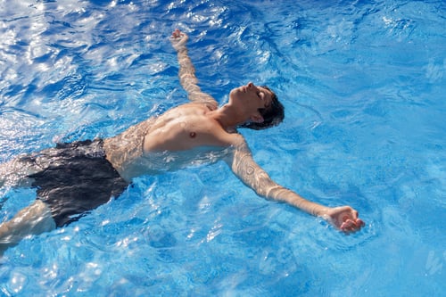 Preview: Relaxed male drifting in bright blue pool water, enjoying sunny day