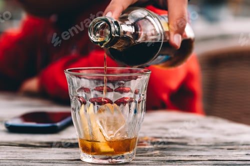 Preview: Close up of hand of woman serving a glass of cola on wooden table