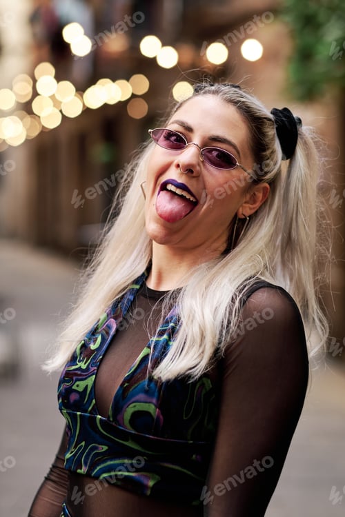 Preview: Alternative woman making a face sticking out her tongue while posing outdoors in the street.